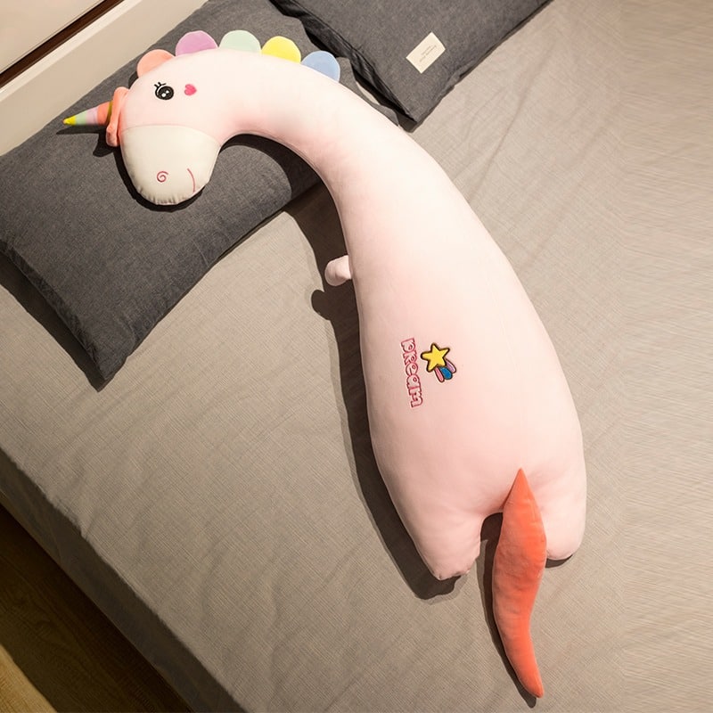 Une peluche licorne rose allongée sur un lit.