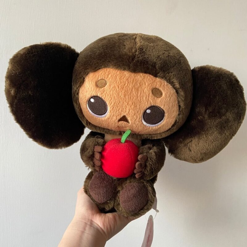 Peluche singe Tchebourachka moelleuse prise par main et fond ecran gris