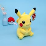 Peluche Pikachu douce jaune assise devant un arrière plan blanc.
