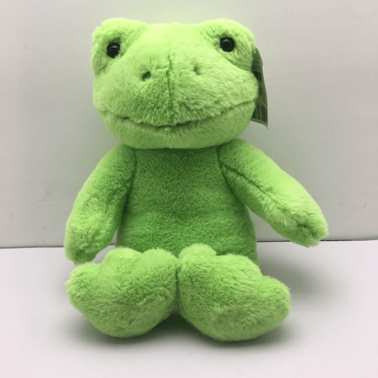 Peluche grenouille verte sur une surface blanche devant un mur blanc.