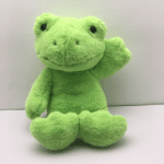 Peluche grenouille verte sur une surface blanche devant un mur blanc.
