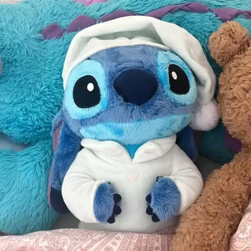 Peluche le chef Stitch avec son chapeau blanc et sa tenue blanche dans une couette à motif rouge.