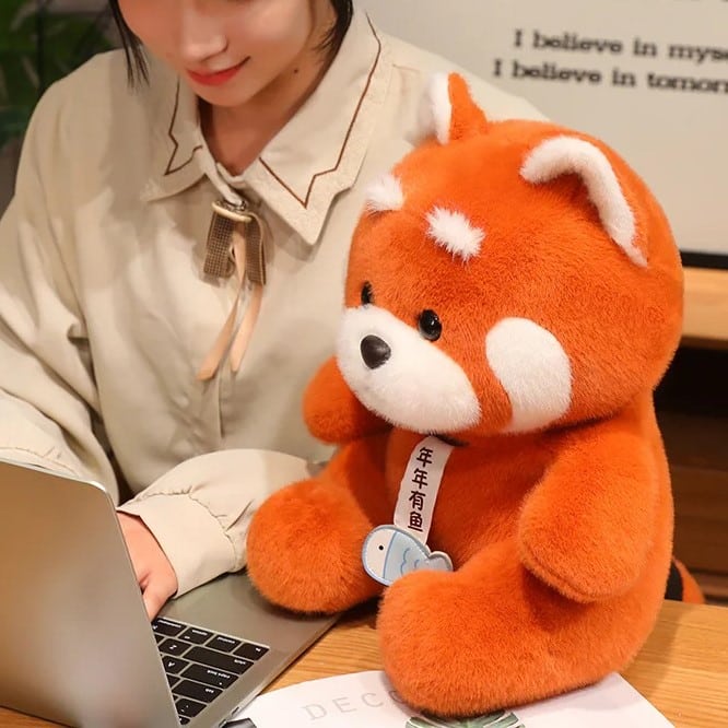 Peluche panda roux sur un bureau avec une femme devant un ordinateur